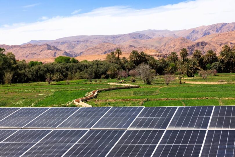 “Solar panels with farmland and mountains in the background, representing renewable energy and sustainable agriculture