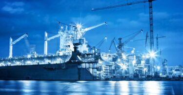 Shipyard at night with cranes and vessels under construction, representing innovation in maritime engineering.
