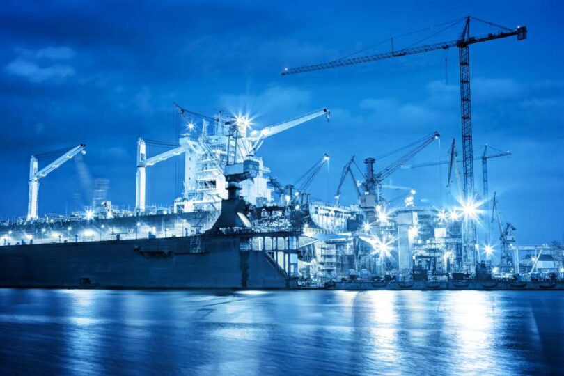 Shipyard at night with cranes and vessels under construction, representing innovation in maritime engineering.