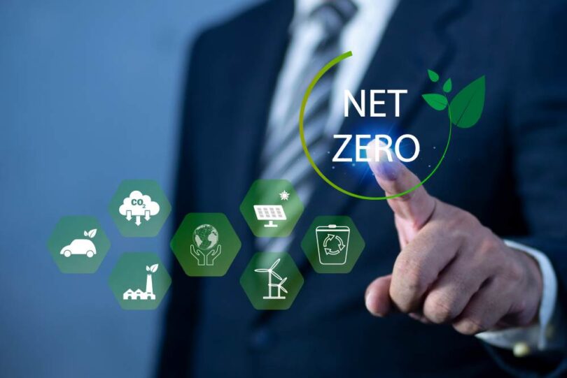 Business professional touching a digital Net Zero icon with renewable energy and sustainability symbols.