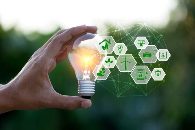 Hand holding a glowing light bulb with green energy and sustainability icons symbolising renewable technology innovation.