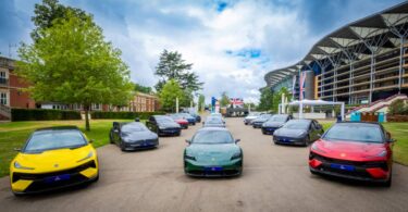 A fleet of electric vehicles lined up outdoors in front of a large event venue, including models from multiple manufacturers in various colours.