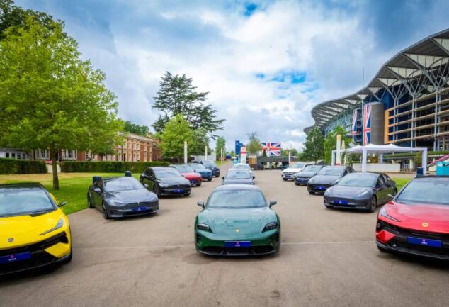 A fleet of electric vehicles lined up outdoors in front of a large event venue, including models from multiple manufacturers in various colours.
