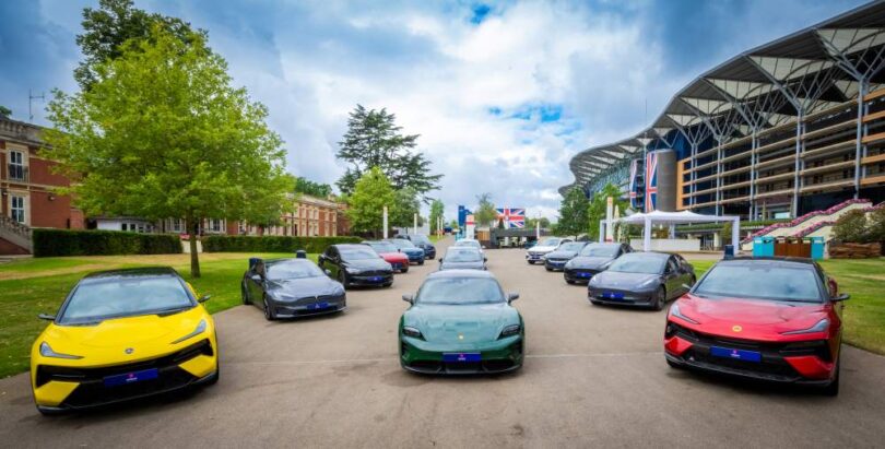 A fleet of electric vehicles lined up outdoors in front of a large event venue, including models from multiple manufacturers in various colours.