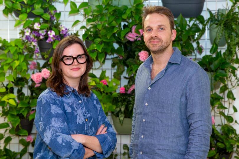 Kuppa co-founders standing in front of an indoor plant wall after the company’s acquisition by Octopus Energy.