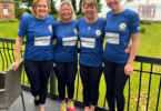 Four members of the Scotland the Wave rowing team standing together in matching blue shirts ahead of their Atlantic rowing challenge.