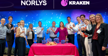 Team members from Norlys and Kraken celebrating their new partnership, standing behind a ceremonial table at a launch event.