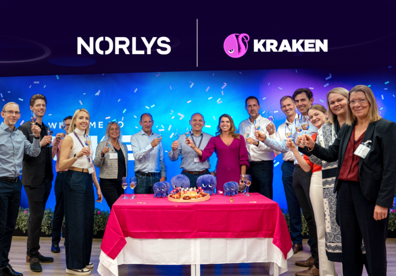 Team members from Norlys and Kraken celebrating their new partnership, standing behind a ceremonial table at a launch event.