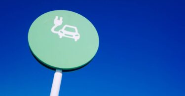 EV signage showing electric vehicle charging symbol on roadside sign against blue sky