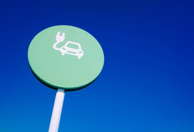 EV signage showing electric vehicle charging symbol on roadside sign against blue sky