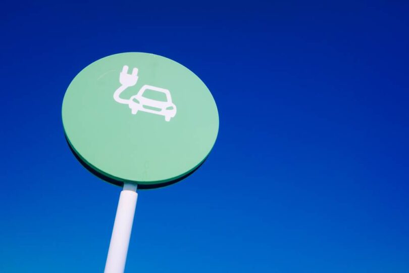EV signage showing electric vehicle charging symbol on roadside sign against blue sky