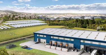 Aerial visualisation of an industrial site showing Caldera thermal-storage heat-battery units beside a warehouse, with an adjacent solar farm