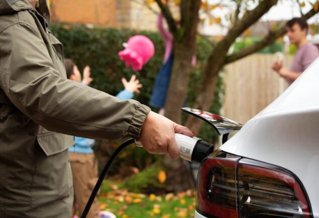 Driver charging an electric vehicle at home, representing the continued growth of electric vehicle adoption in the UK.