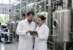 Technicians reviewing data beside stainless steel fermentation tanks in a modern biomanufacturing facility