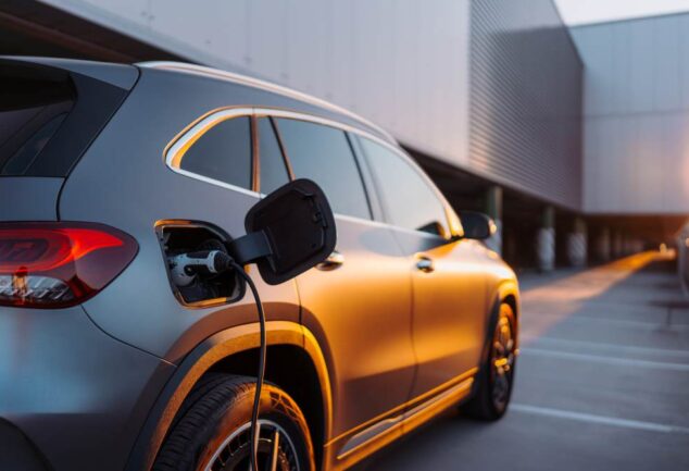 Electric car charging outside a modern building during sunset