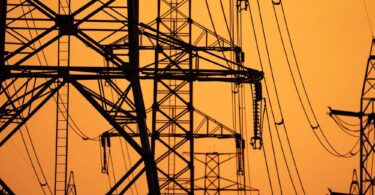 High-voltage electricity transmission towers supporting Europe's power grid infrastructure at sunset.