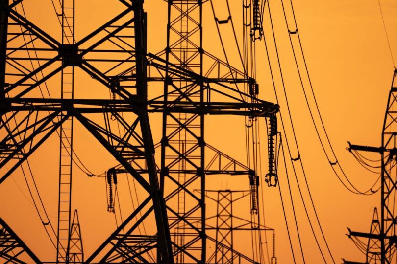 High-voltage electricity transmission towers supporting Europe's power grid infrastructure at sunset.