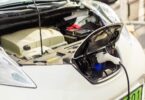 Electric car plugged into a charging station with the bonnet open, showing EV battery and charging components.