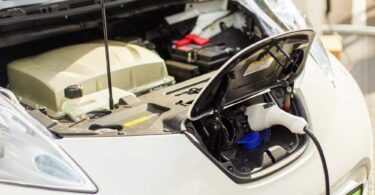 Electric car plugged into a charging station with the bonnet open, showing EV battery and charging components.