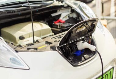Electric car plugged into a charging station with the bonnet open, showing EV battery and charging components.