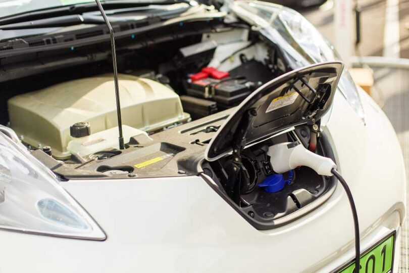 Electric car plugged into a charging station with the bonnet open, showing EV battery and charging components.