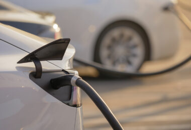 Electric cars charging at an outdoor charging station at sunset.