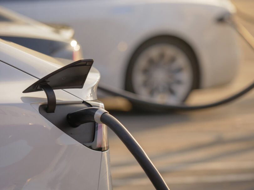 Electric cars charging at an outdoor charging station at sunset.