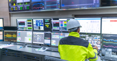 Engineer and technician in a control room monitoring a program across multiple computer screens