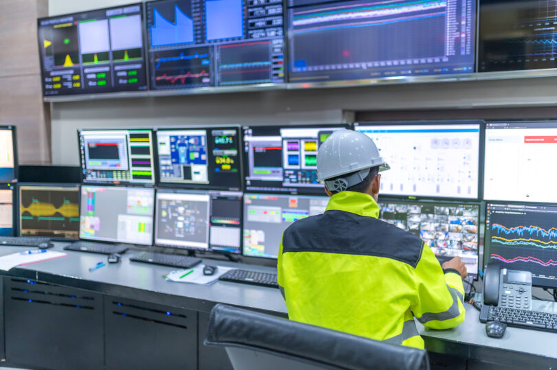 Engineer and technician in a control room monitoring a program across multiple computer screens