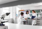 Group of smiling scientists in a laboratory, one holding a folder, discussing a report together.