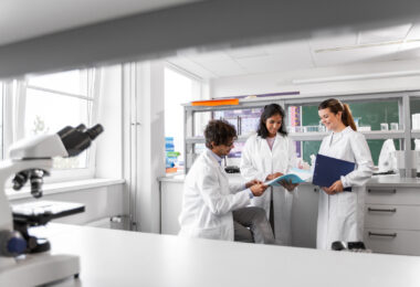 Group of smiling scientists in a laboratory, one holding a folder, discussing a report together.