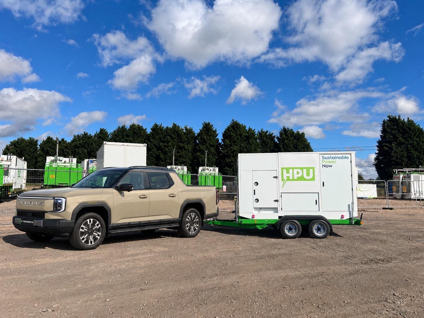 Tan Maxus Terron 9 pickup truck towing a white trailer-mounted HPU unit marked "Sustainable Power Now" on a gravel site