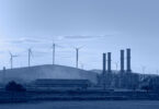 Silhouette of a natural gas processing plant alongside wind turbines generating electricity.
