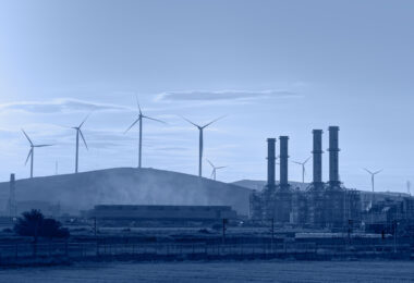 Silhouette of a natural gas processing plant alongside wind turbines generating electricity.