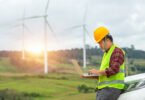 Engineer inspecting a wind turbine at a construction site, with a car parked nearby for site access.