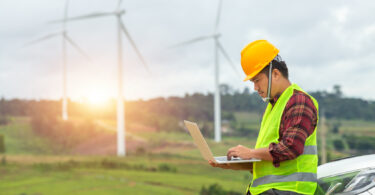 Engineer inspecting a wind turbine at a construction site, with a car parked nearby for site access.
