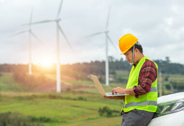 Engineer inspecting a wind turbine at a construction site, with a car parked nearby for site access.
