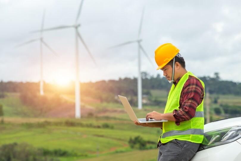 Engineer inspecting a wind turbine at a construction site, with a car parked nearby for site access.