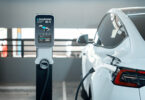An electric car plugged in to charge in a city shopping centre parking lot, shown with a green energy theme.
