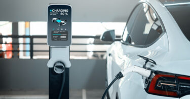 An electric car plugged in to charge in a city shopping centre parking lot, shown with a green energy theme.