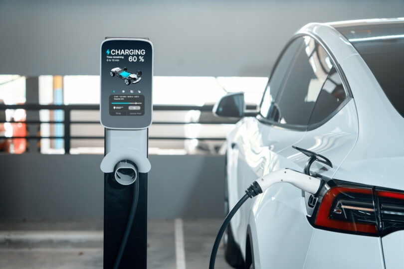 An electric car plugged in to charge in a city shopping centre parking lot, shown with a green energy theme.