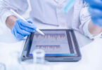 A woman in a laboratory setting writing notes on a document, appearing to be a scientist or doctor at work.