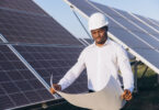 An engineer inspects solar panels at a solar farm while reviewing a blueprint.
