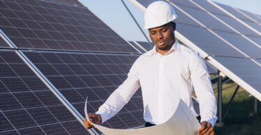 An engineer inspects solar panels at a solar farm while reviewing a blueprint.