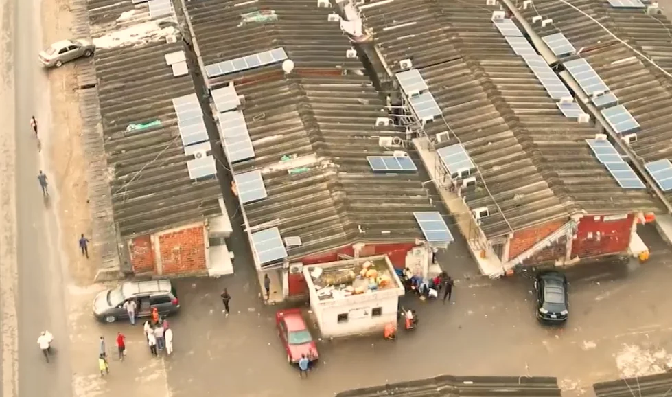 Aerial view of corrugated market rooftops with solar panels and air conditioners, with parked cars and people below